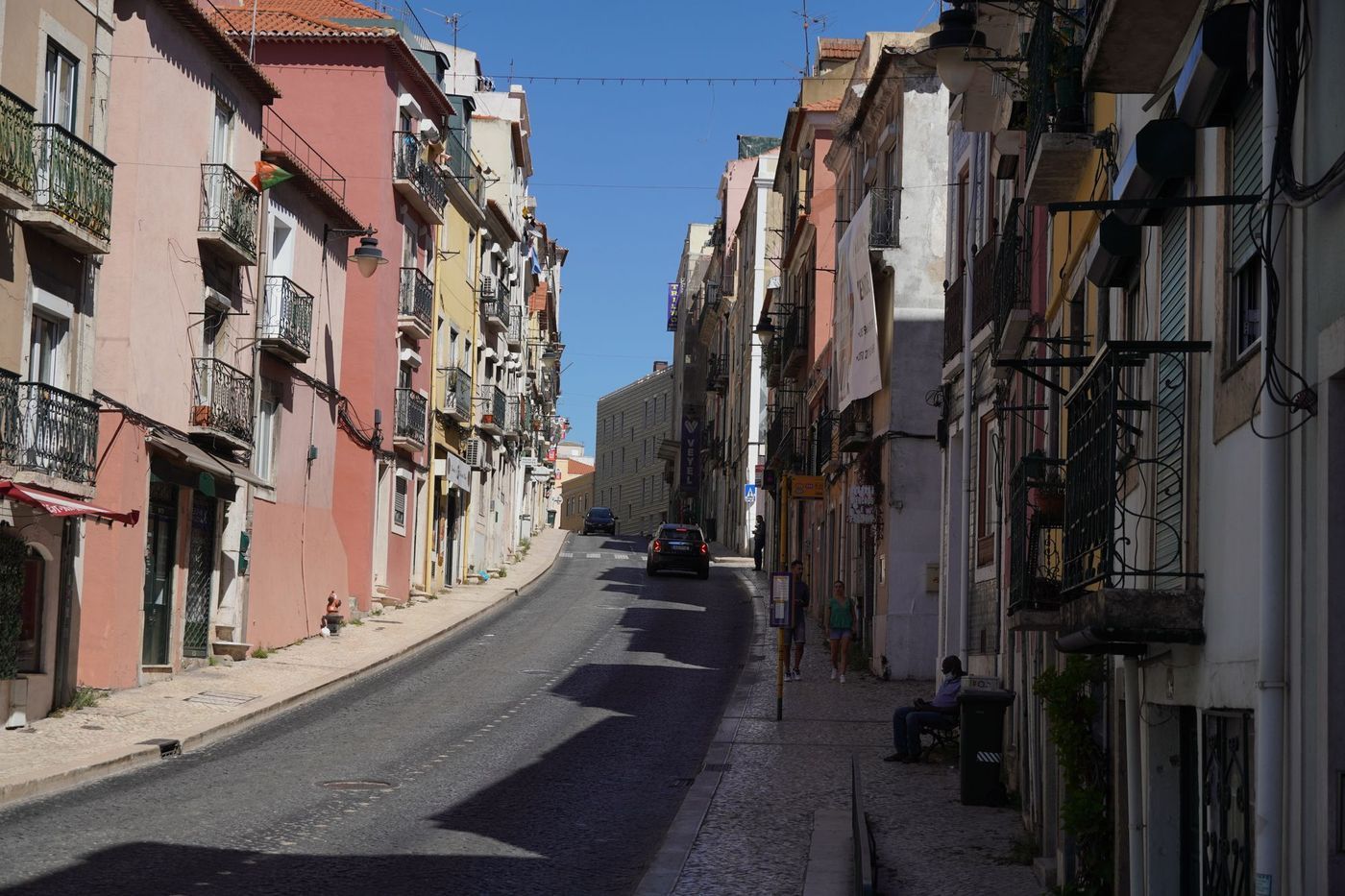 A sunlit hillside street of pastel townhouses in Lisbon, one end of a Bromley to Portugal move