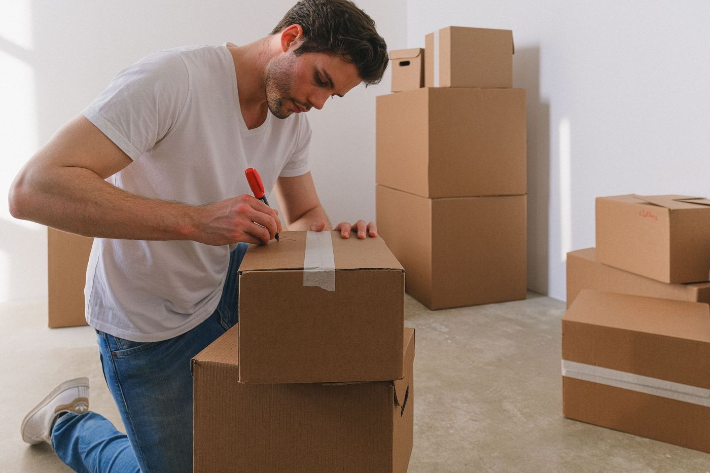 A man kneeling to label a packed moving box with a marker