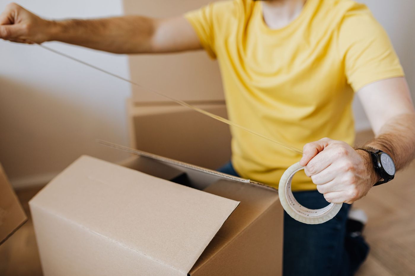 A man sealing a packed cardboard box with tape